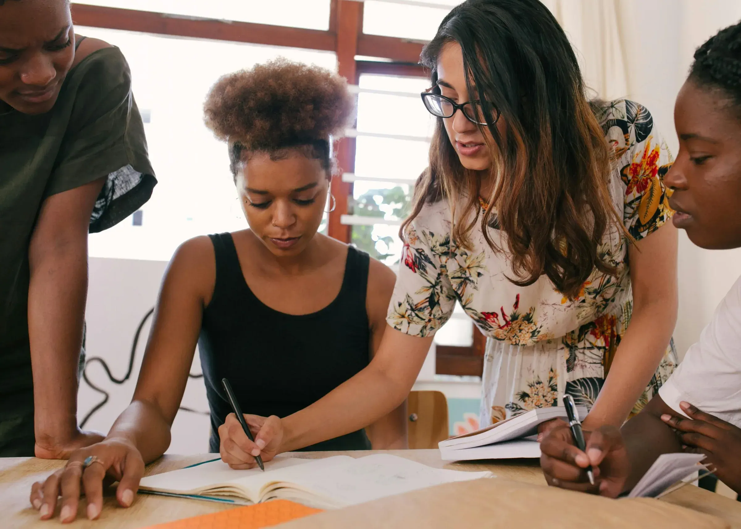 Four young women working together around a table, notebooks open.