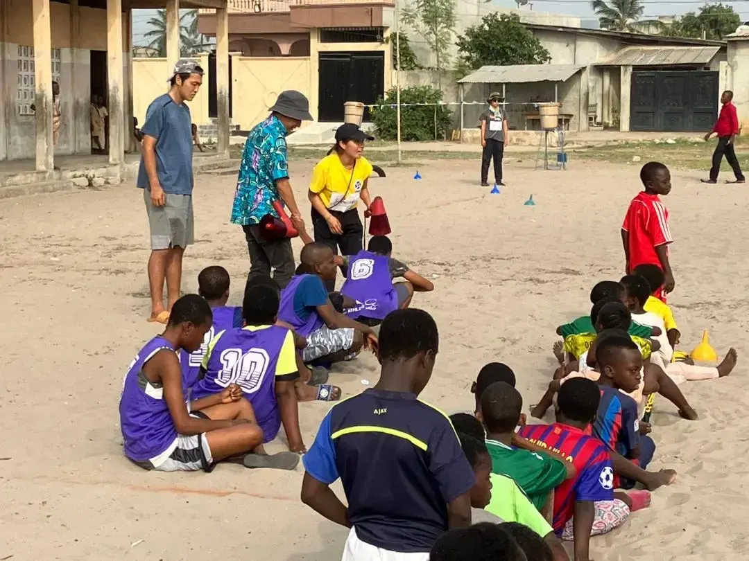 Children sitting on the sand during a game led by volunteers.
