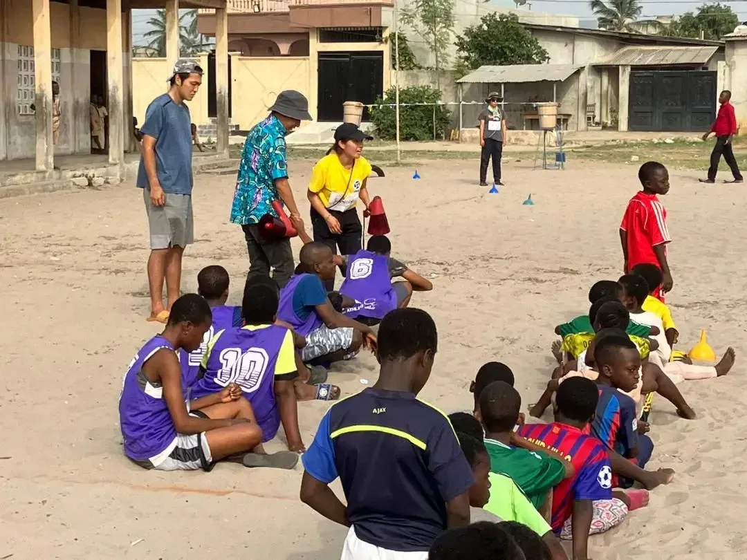 Children sitting on the sand during a game led by volunteers.